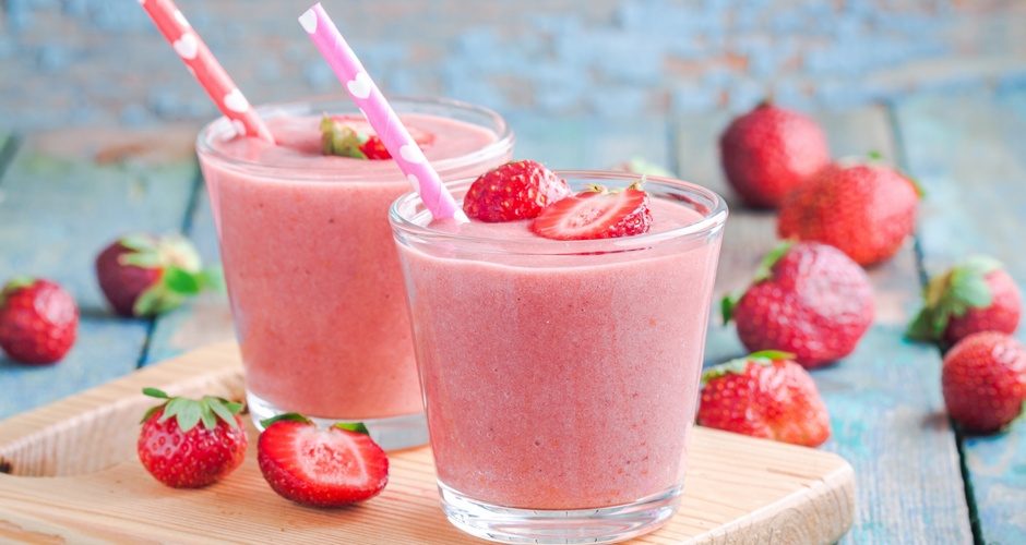 Two glasses of strawberry smoothie with straws on a wooden board
