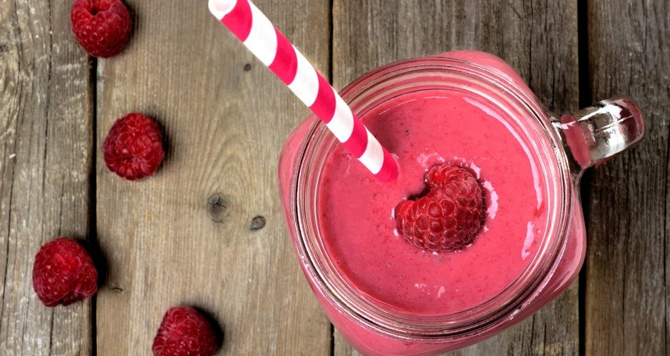 Pink raspberry smoothie in a mason jar with straw, overhead view on rustic wood background