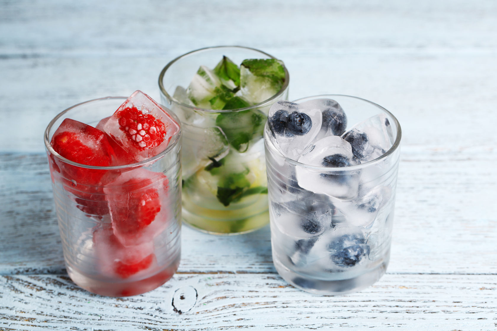 30502713 - ice cubes with mint leaves, raspberry and blueberry in glasses, on color wooden background
