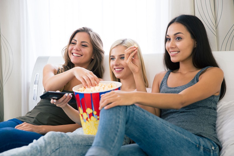 46468406 - portrait of a three happy girlfriends eating popcorn and watching tv at home