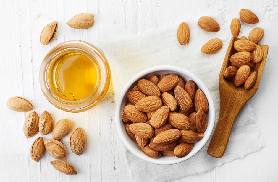 55245854 - almond oil and bowl of almonds on white wooden background. top view