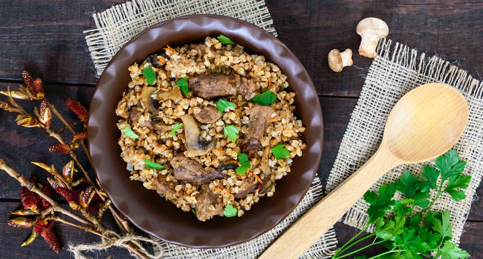 77481918 - buckwheat porridge with pieces of meat and mushrooms on a dark wooden background. top view.